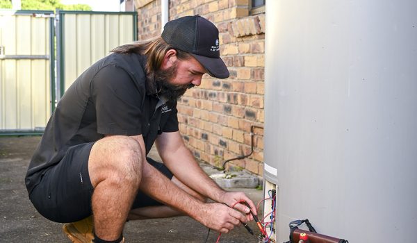 Emergency electrician Loganholme technician inspecting a hot switchboard at night with a head torch while a worried homeowner looks on.