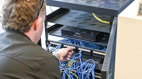 Electrician completing smoke alarm installation Loganholme, fitting a new white photoelectric alarm to a hallway ceiling in a family home.