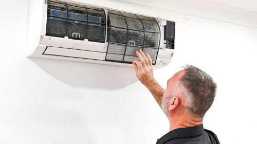 Electrician completing ceiling fan installation Loganholme, adjusting a modern white fan in a family living room.